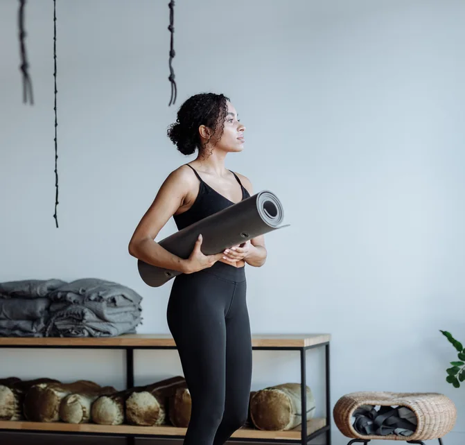 Black woman holding a yoga mat in a studio