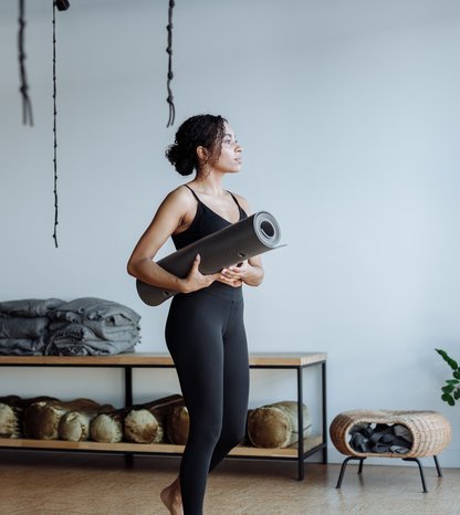 Black woman holding a yoga mat in a studio