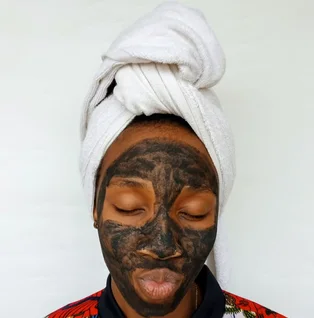 Black woman applying a clay skincare mask