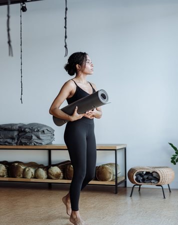 Black woman holding a yoga mat in a studio